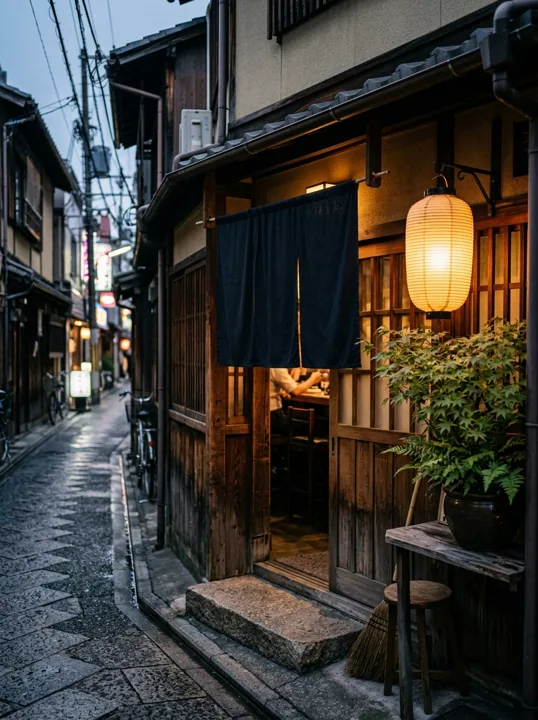 路地に面した店の入口。紺の暖簾と提灯が灯っている
